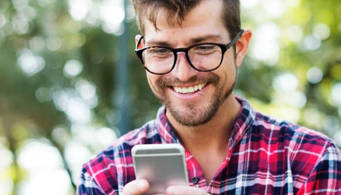 homem de óculos sorrindo enquanto olha para o smartphone